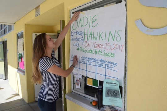 Senior Emily Angiolini hangs a poster advertising the 2017 Mira Costa Sadie Hawkins Dance during lunch on Thursday near the East Locker Hall. ASB announced the dance, themed “The Suite Life At Sadies,” will take place on March 25 at the Embassy Suites near LAX.